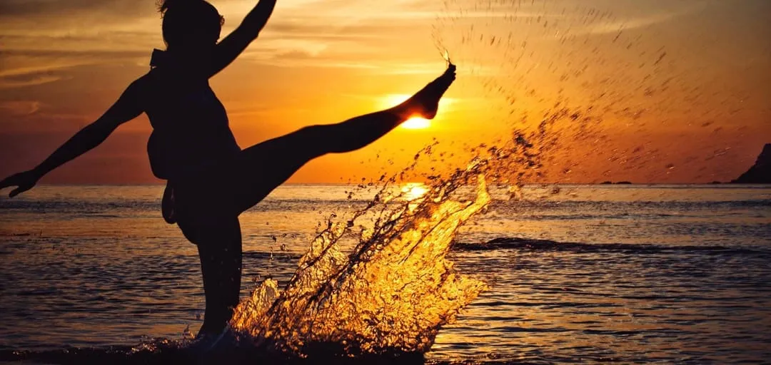 Woman kicking water at sunset